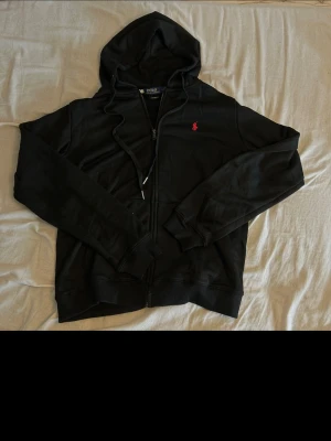 Svart Ralph Lauren zip - En svart Ralph Lauren Zip med röd logga. Storlek M (~178-184) bra passform. Snygg tröja till skolan eller finare tillfällen. Säljer åt en vän. Helt ny bara testanvänd men inget som föll han i smaken. Så han säljer den. All konsversation sker från min vän. 