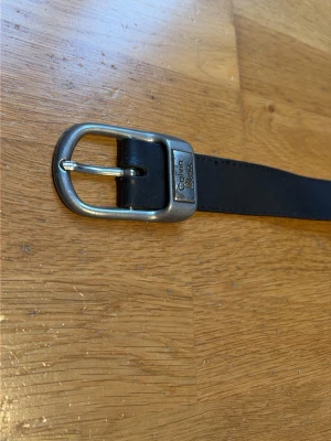 Vintage brunt svart skärp från Calvin Klein Jeans - Snyggt svart skärp från Calvin Klein Jeans med präglad logga längs remmen och metallspänne med märkets namn. Klassisk design som passar till jeans eller byxor. Tillverkat i skinn för en stilren look.