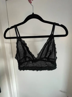 Svart spet-bh med smala axelband - En svart, transparent spets-bh med smala axelband och dekorativ spetskant runt hela 