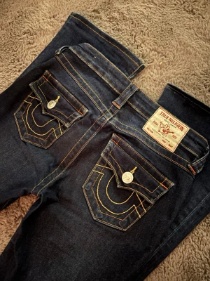 True Religion Becca Bootcut Jeans - Mörkblå jeans från True Religion, modell BECCA Mid Rise Bootcut. Klassisk bootcut-passform med kontrastsömmar och ikoniska fickdetaljer. Inga som helst defekter. Bara att höra av sig om det finns frågor💗💗 Säljer pga att dom inte kommer till användning💕