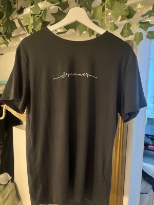 Grå t-shirt med texten dreamer - Säljer en grå t-shirt med vit text 'dreamer' på bröstet. Klassisk rund halsringning och korta ärmar. Skön och enkel modell som passar till det mesta. Materialet känns mjukt och troligtvis i bomull.