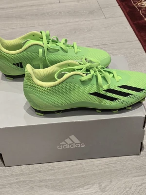 Limegröna Adidas fotbollsskor - Säljer ett par limegröna Adidas fotbollsskor med svarta detaljer och snörning. Skorna har en lätt mesh-överdel och dobbar för bra grepp på planen. Perfekta för dig som vill sticka ut på matchen!