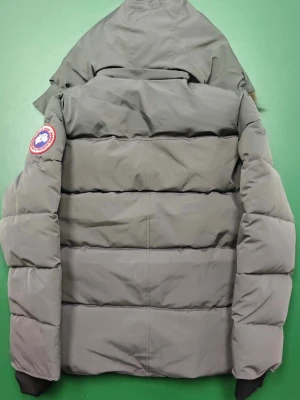 Grå Canada Goose pufferjacka M - Säljer en grå pufferjacka från Canada Goose med avtagbar huva och fuskpäls. Jackan har klassisk patch på ärmen, stora fickor och stängs med både dragkedja och knappar. Perfekt för kalla dagar och riktigt snygg till vinterlooken.