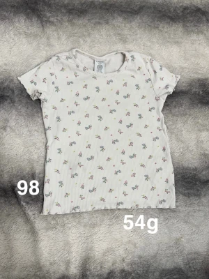 Vit blommig t-shirt från Lindex - Supersöt vit t-shirt från Lindex med små blommor. T-shirten har korta ärmar. Perfekt för vår och sommar, enkel att matcha till allt!🌸 Fint använt skick. Storlek 98