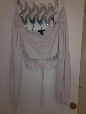 Ljusbeige offshoulder topp Amisu - Trendig ljusbeige offshoulder topp från Amisu i ribbad bomullsmix. Toppen har långa puffiga ärmar, croppad passform och snygg snörning framtill med cut out-detalj under bysten. Perfekt till höga jeans eller kjol.