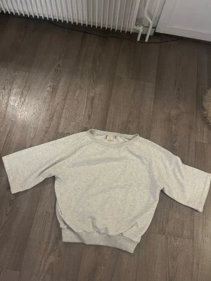 Ljusgrå sweatshirt från Nelly - Ljusgrå sweatshirt från Nelly med rund halsringning och trekvartsärm. Tröjan har en relaxed passform och ribbade muddar vid hals och nederkant. Perfekt för en chill och enkel stil.