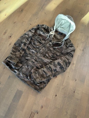 Camouflage jacka med huva - Säljer en camouflagefärgad parkajacka från Divided med grå huva och snörning. Perfekt för dig som gillar streetwear eller är jävligt grisch! Pris går att diskutera