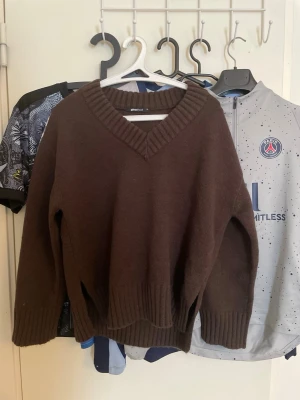 Brun stickad v-ringad tröja Gina Tricot - Mysig brun stickad tröja från Gina Tricot med bred v-ringning och ribbade muddar vid ärmslut och nederkant. Perfekt för lager på lager och chill höst- eller vinterstil. Passar dig som gillar en enkel men ändå snygg look. Aldrig använt!