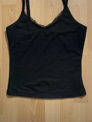 Två tunna linnetoppar i svart och vit - Två tunna linnetoppar som är ribbade med spetskant upptill i svart och vit, topparna är figurnära och stretchiga.