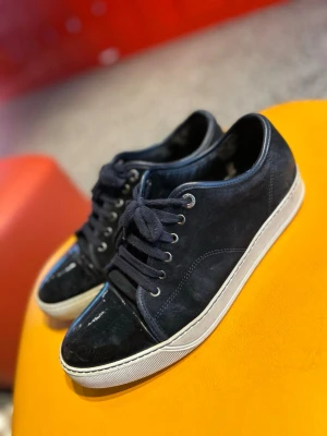 Lanvins - Säljer ett par svarta sneakers med ovandel i mocka och snygg lackad tå. Skorna har vita sulor, svarta skosnören och metallfärgade öljetter. Perfekta för dig som gillar en clean men ändå unik look.