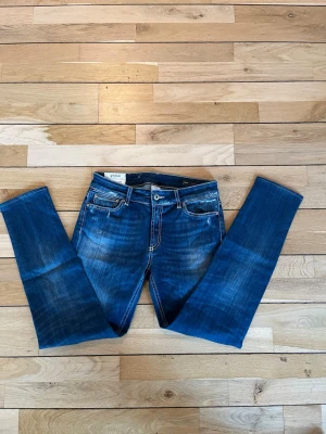 Blå distressed jeans från Dondup - Säljer ett par blå jeans från Dondup, modell Tara. Jeansen har snygga slitningar och en tvättad look med kontrastsömmar. Klassisk femficksmodell och normal passform. Tillverkade i Italien och gjorda i jeansmaterial.