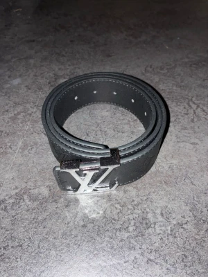 Louis Vuitton bälte - Säljer ett svart bälte från Louis Vuitton med klassiskt LV-spänne i silverfärg. Bältet är gjort i skinn och har präglade LV-loggor längs hela bandet. Perfekt accessoar för att lyfta vilken outfit som helst.