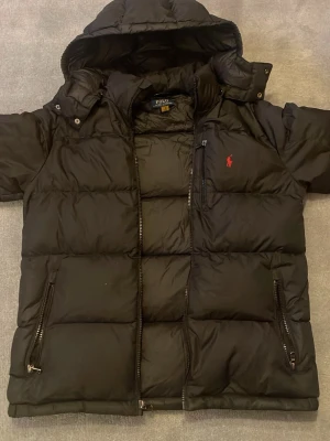 Polo jacka - Svart pufferjacka från Polo Ralph Lauren med avtagbar huva. Den är XL barn storlek som passar som S för vuxen storlek. OBS! lappen är borta som du kan se i sista bilden.