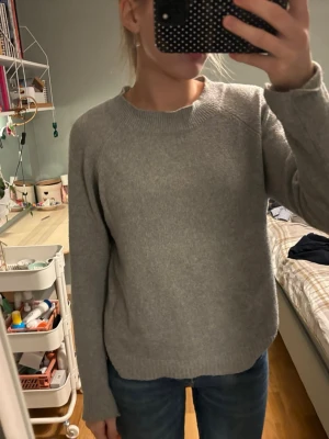 Grå stickad tröja med rund hals - En enkel och stilren grå stickad tröja med rund halsringning och långa ärmar. Perfekt att slänga på sig när det är kyligt ute. Tröjan har en klassisk passform och ribbade muddar vid ärmslut och nederkant.