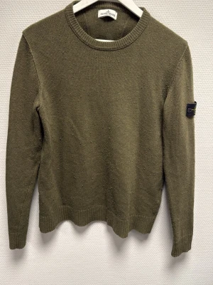 Olivgrön stickad tröja Stone Island - Säljer en olivgrön stickad tröja från Stone Island Junior med klassisk patch på ärmen. Tröjan har rund hals, ribbade muddar och lång ärm. Perfekt för dig som gillar streetwear och vill ha något stilrent men ändå ikoniskt. 100% äkta. Nypris ca 2500-3000kr. Skriv för frågor!