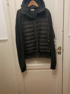 Mörkgrön Moncler cardigan  - Säljer en mörkgrön cardigan från Moncler med stickade ärmar och detaljer. Jackan har huva, dragkedja framtill och fickor på ärmen. Perfekt för dig som vill ha en snygg och funktionell jacka med streetkänsla och exklusiv vibe.