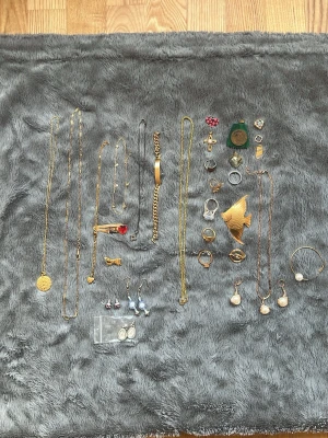 Samling vintage smycken i guldton - Säljer en mix av vintage smycken i guld- och silverton, inklusive halsband, armband, örhängen och broscher. Flera hängen med pärlor, hjärtan och fiskmotiv samt detaljer som kors, stenar och polerade ytor. Perfekt för dig som gillar unika accessoarer och vill sticka ut.