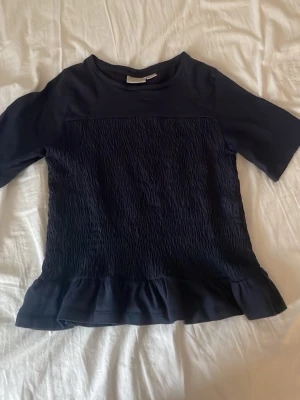 Mörkblå blus med volangkant - Säljer en mörkblå blus med korta ärmar och rund hals. Säljer den för att den har blivit för liten för mig. Pris kan diskuteras.