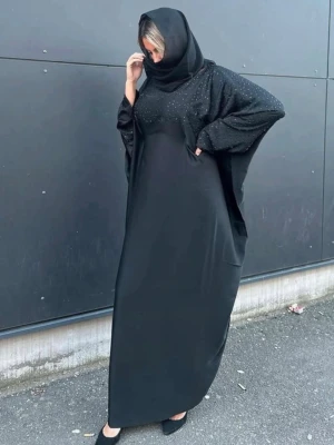 Svart abaya med glittriga detaljer - Säljer en svart abaya med glittriga detaljer upptill och på ärmarna. Abayan har en lös passform och vida ärmar, perfekt för dig som gillar en modest och elegant stil. Materialet känns mjukt och faller snyggt. Snygg till både vardagliga och speciella tillfällen. Köpt för 600kr säljer för 350kr