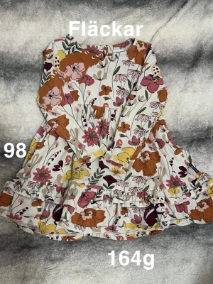 Blommig långärmad klänning Polarn o pyret - Supersöt långärmad klänning från Polarn o pyret med färgglatt blommönster i vitt, rosa, gul, brun och grön. Klänningen har volangdetaljer och en lekfull look, perfekt för vår och sommar.🌸 Fläckar. Storlek 98