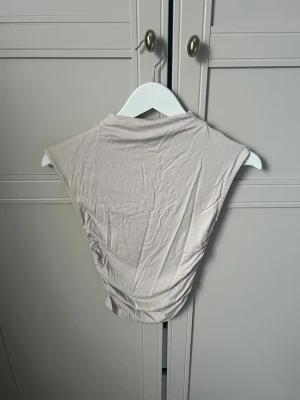 Beige ärmlös topp Gina Tricot XS - Säljer en beige ärmlös topp från Gina Tricot i storlek XS. Toppen har en enkel, clean design med hög hals och lätt rynkade sidor. 