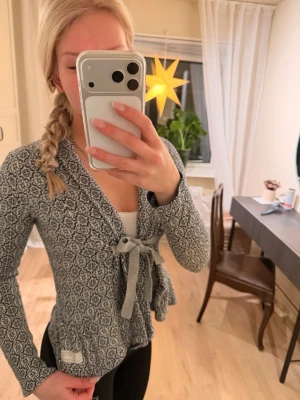 Mönstrad kofta från Odd Molly med knyt - Denna klassiska, supersöt blå och vit mönstrad kofta från Odd Molly med knytband i midjan och volangkant nedtill. Koftan har långa ärmar och är stickad i mjukt material. Koftan är för liten för mig på bilderna. Väldigt fint skick, sällan använd