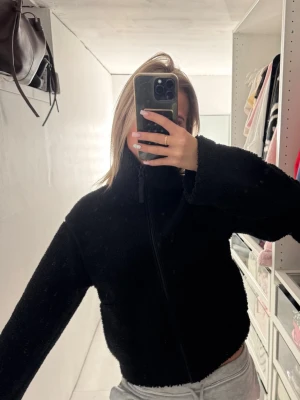 Svart teddyjacka med dragkedja - Mysig svart teddyjacka med hög krage och hel dragkedja framtill. Jackan har en loose passform och är perfekt för kyliga dagar. Tillverkad i mjukt fleece-liknande material som ger en skön och avslappnad look.