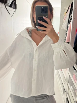 Vit skjorta - Säljer en vit, luftig skjorta med krage och knappar framtill. Skjortan har långa, vida ärmar med knapp vid ärmslut och är tillverkad i ett tunt, lätt material som ger en avslappnad vibe. Perfekt för varmare dagar eller lager-på-lager.