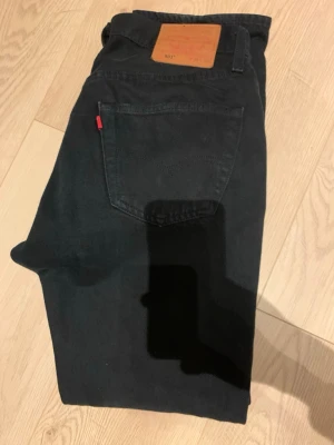 Svarta Levi's 501 jeans - Säljer ett par klassiska svarta Levi's 501 jeans med raka ben och femficksmodell. Jeansen har den ikoniska röda Levi's-lappen på bakfickan och patch i läder bak i midjan. Tillverkade i slitstarkt bomullstyg och passar perfekt till en avslappnad stil.