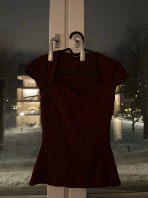 Vinröd ribbad topp från Anna Field - Säljer en vinröd topp från Anna Field med ribbad struktur och snygg v-ringad urringning. Modellen är figurnära med korta ärmar och stretchigt material som sitter bekvämt. Perfekt till jeans eller kjol för en trendig look.