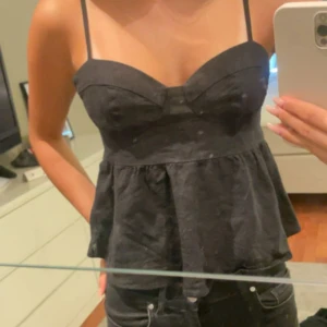 Svart linnetopp med tunna axelband - Säljer en svart topp med tunna axelband och markerad byst. Toppen har en lätt utsvängd nederdel. Perfekt att matcha med jeans eller kjol.