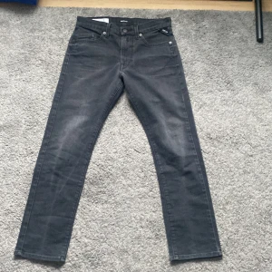 Replay Mini Waitom svarta jeans - Snygga svarta jeans från Replay, modell Mini Waitom. Klassisk femficksdesign med raka ben och diskreta detaljer. Jeansen har en mörk tvätt och är tillverkade i mjukt denim-material med knappstängning och bälteshällor. Perfekt för dig som gillar stilrena och tidlösa jeans.