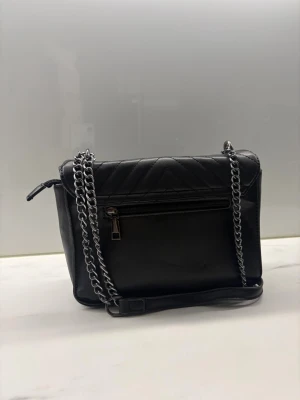 Svart quiltad axelväska från YSL - Säljer en svart quiltad axelväska från YSL med silverfärgad kedja och YSL-logga framtill. Väskan är tillverkad i skinn och har ett snyggt mönster med diagonala linjer. Utrustad med dragkedja på baksidan och justerbar axelrem.