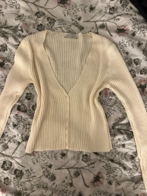 Ribbad beige kofta  - Säljer en beige ribbad kofta från Shade med djup v-ringning och långa ärmar. Koftan har knappar framtill och är tillverkad i ett mjukt stickat material som sitter snyggt på kroppen. Perfekt att styla med jeans eller kjol.