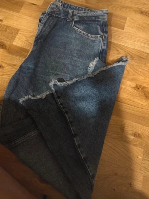 Blå jeans med fransad kant - Säljer ett par blå jeans med fransad kant längs benen. Klassisk femficksmodell med knapp och dragkedja i midjan. Jeansen har en rak passform och är tillverkade i jeansmaterial. Perfekt för dig som gillar en lite råare stil.