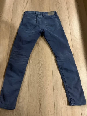 Replay Anbass mörkblå jeans - Säljer ett par Replay Anbass jeans i mörkblå färg med klassisk femficksdesign och smal passform. Jeansen har en snygg tvätt och är tillverkade i mjukt bomullsmaterial med lite stretch för extra komfort. Perfekt för dig som gillar stilrena och moderna jeans.