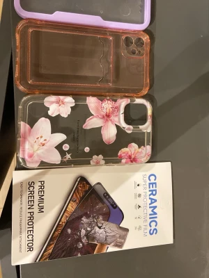 iPhone 11 Skal & Skärmskydd  - Flera skal till iPhone 11: ett lila stöttåligt skal med dubbel sida för att undvika kladdiga fingrar efter du tex ätit chips, ett transparent med blommor och text, ett ljus rosa med kortfack samt ett keramiskt skärmskydd. Alla i gott skick, inga synliga defekter. Perfekt för att skydda och ge din mobil en personlig touch.