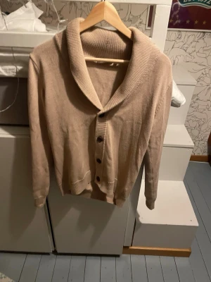 Beige kofta från RYVLS Stockholm - Säljer en beige kofta från RYVLS Stockholm i storlek 158/164. Koftan har en bred, ribbad sjalkrage och stängs med fyra knappar framtill. Långärmad och i mjukt stickat material, perfekt för lager på lager under kyliga dagar. Skriv vid minsta fundering. Pris kan diskuteras 