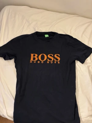 Svart t-shirt från Hugo Boss - Snygg svart t-shirt från Hugo Boss med stor orange logga på bröstet. Klassisk rund hals och korta ärmar. Perfekt för dig som gillar stilrena plagg med tydlig branding.