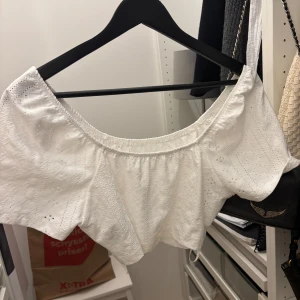 Vit offshoulder croppad blus - Säljer en vit blus med offshoulder och croppad passform. Blusen har broderade detaljer och är tillverkad i bomull. Perfekt för sommarens alla tillfällen, med luftig och söt design.