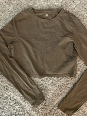 Beige croppad långärmad topp 157 - Säljer en beige croppad långärmad topp från 157 i storlek S. Toppen har rund halsringning och är tillverkad i mjuk bomull med lite elastan för extra stretch. Perfekt att styla med jeans eller kjol för en chill look.