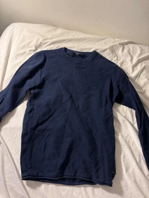 Mörkblå stickad tröja från Selected - Säljer en mörkblå stickad tröja från Selected med rund hals och långärmad design. Tröjan har en diskret struktur i materialet och passar perfekt för kyliga dagar. Enkel och stilren modell som är lätt att matcha med jeans eller chinos.