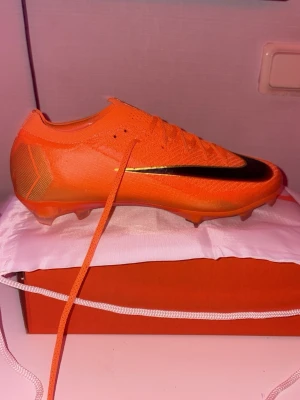 Nike orange fotbollsskor med snörning - Säljer ett par grymt snygga orangea Nike fotbollsskor med svart swoosh på sidan. Skorna har snörning, platt sula med dobbar och är tillverkade i syntetmaterial för bästa grepp på planen. Perfekt för dig som vill sticka ut med färg och stil på matchen.