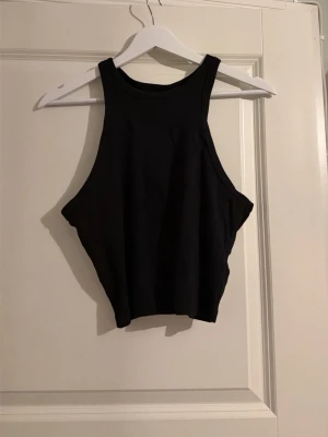 Svart ribbad linnetopp från H&M Divided - Säljer en svart ribbad linnetopp från H&M Divided i storlek L. Toppen har en hög halsringning och är ärmlös med breda axelband. Materialet är mjukt och stretchigt, perfekt för att matcha med jeans eller kjol. 🩷