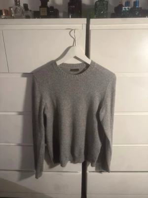 Grå Kashmir tröja från Stenströms - Säljer en stilren grå kashmir tröja från Stenströms. Tröjan har rund halsringning, ribbade muddar och lång ärm. Perfekt för dig som gillar klassisk och enkel design med mjukt material som känns skönt mot huden.