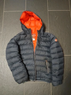 Mörkblå Colmar pufferjacka med huva - Säljer en mörkblå pufferjacka från Colmar.. Jackan har dragkedja framtill och två sidofickor med dragkedja. Perfekt för kyliga dagar. Storlek S.