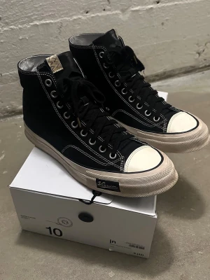 Visvim Skagway High - Säljer ett par svarta höga sneakers från Visvim med kontrasterande vita sömmar och tåparti. Skorna har snörning, rund tå och en beige sula med zigzag-mönster runtom. Materialet är canvas med detaljer i skinn på plösen. Perfekt för dig som gillar streetwear. Fint skick! Nypris: 9500 SEK