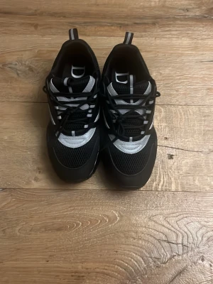 Svarta sneakers med silvriga detaljer - Säljer ett par snygga sneakers i svart med silvriga detaljer och meshpartier. Skorna har rund tå, platt sula och snörning framtill. Märket syns tydligt på sidan och tungan. Perfekta för dig som gillar exklusiva och trendiga sneakers.