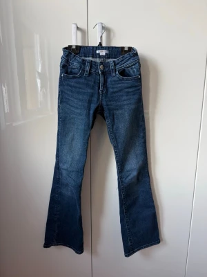 Blå bootcut jeans med fickdetaljer - Säljer ett par blå jeans ifrån Gina tricot med bootcut passform och snygga fickor bak med knappdetaljer. Jeansen är i storlek 152 och är low waist och har justerbar midja.💗