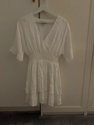 Vit kortklänning från Amisu -  Säljer en vit kortklänning från Amisu i storlek 32 som är köpt från New Yorker. Klänningen har v-ringad hals, korta volangärmar och är lite tajtare i midjan. Tyget är ganska tunt och luftigt, perfekt till sommaren. Är endast använd en gång. 